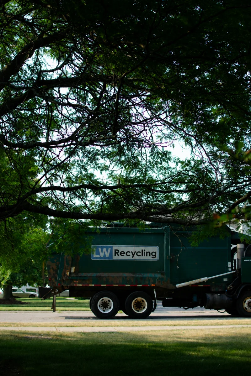 LW Recycling vehicle for skip hire and waste collection parked beneath trees.